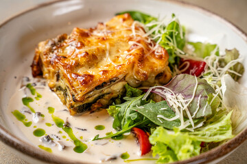 Closeup of lasagna with salad and creamy sauce