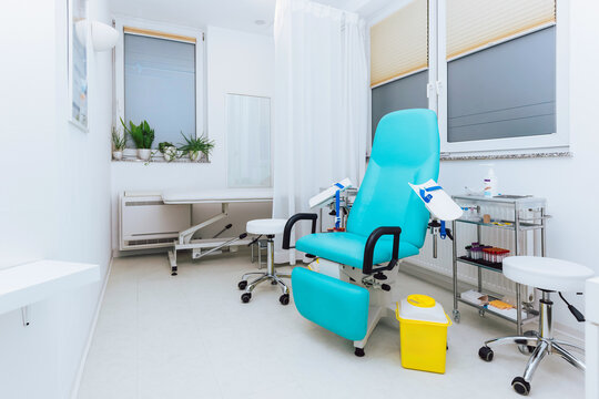 A bright laboratory clinic room features a teal chair for patient blood test or blood donation next to medical supplies and plants by the window.