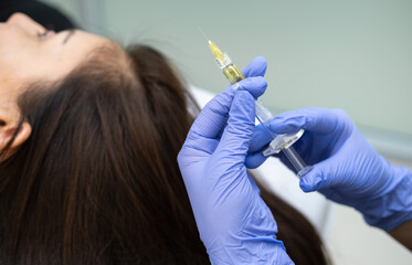 Caucasian female mature patient getting head or scalp injection in cosmetology clinic. Receding hairline, baldness problems, hairloss. Cosmetologist doing injections with syringe. 