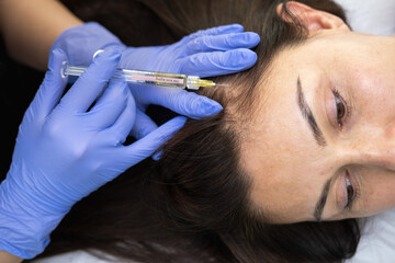 Caucasian female mature patient getting head or scalp injection in cosmetology clinic. Receding hairline, baldness problems, hairloss. Cosmetologist doing injections with syringe. 