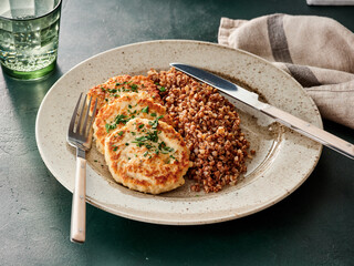 Delicious chicken patties are plated alongside fluffy buckwheat. This wholesome meal is ideal for a simple lunch or dinner at home, enjoyed in a cozy kitchen setting