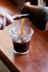 Pouring steaming hot coffee into plastic cup on windowsill