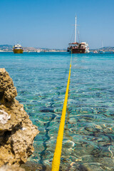 Vertical Low-Angle View of a Yellow Rope in Crystal Clear Water Leading to Large Touristic Boats near Vardiani Island, Kefalonia