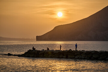 Rocky coastline sunset golden hour Mediterranean sea people silhouette Calpe Spain horizontal seascape dramatic lighting natural landscape