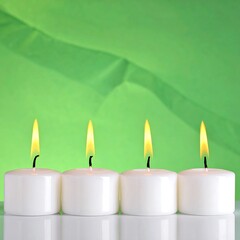 Four white tea light candles with flames against a blurred green background