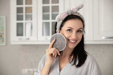 A beautiful adult woman cleanses her face at home, selective focus. Portrait of a woman with a skincare sponge. Real photo.