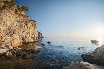 The image captures a breathtaking view of rocky cliffs overlooking a serene blue sea at sunrise. West coast of the Gulf of Antalya in southern Turkey. High quality photo
