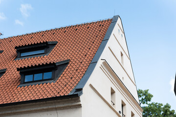 Steep gable roof with red ceramic tiles and black-framed windows on a white building under clear blue sky. Suitable for architecture, construction, roofing, and real estate design reference.