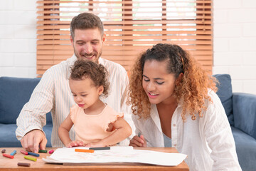 Happy parents playing with their adorable baby at home. Mom and dad looking at their baby who drawing on paper with pencil in cozy living room. Creative education. Early development