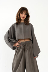 Confident young woman posing in gray wide sleeve crop top and wide trousers, studio fashion.