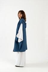 Elegant young woman in white wide sleeve outfit and long hooded blue vest, side profile.