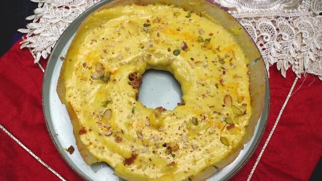 Malai Ghevar, famous sweet or Rajasthan India, serve on a red background. Ghewar having creamy yellow topping with nuts