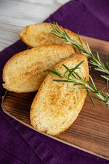 sliced and toasted French baguette on a board with a sprig of rosemary