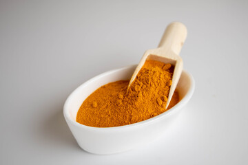 ground turmeric in a wooden spoon on white background
