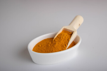 ground turmeric in a wooden spoon on white background