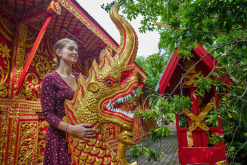A Young Woman Embraces a Beautifully Crafted Golden Dragon Sculpture at a Vibrant Temple Surrounded by Lush Greenery and Intricate Architectural Details