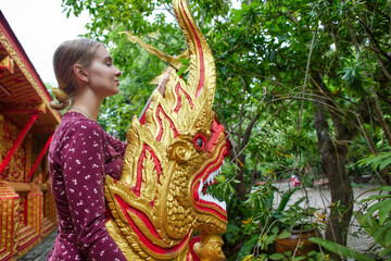 A Young Woman Interacts with a Vibrantly Carved Mythical Creature Amidst Lush Greenery in a Peaceful Outdoor Setting