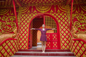 Obraz premium A Joyful Young Woman Poses Gracefully at the Entrance of a Vibrantly Decorated Temple with Rich Red and Golden Details