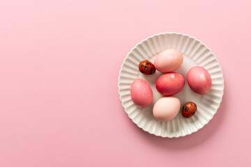A collection of beautifully dyed Easter eggs in various shades rests on a decorative plate, set against a soft pink background, celebrating the joyful holiday spirit