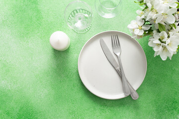 A lovely spring table setting features a white plate, silverware, and elegant glassware, complemented by fresh flowers and a soft green background, perfect for gatherings and meals