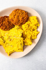 A vibrant plate features fluffy yellow rice, creamy rhubarb fried eggs, and crispy meat fritters, showcasing a hearty and flavorful meal perfect for any time of the day