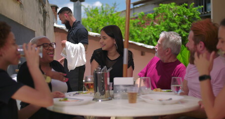 Family and friends enjoying laughter and food at a backyard lunch, cheerful and casual atmosphere...