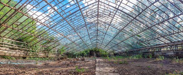 Empty abandoned greenhouse with metal frame, broken windows and rusty pipes. View from entrance.