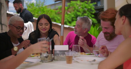 Family and friends enjoying laughter and food at a backyard lunch, cheerful and casual atmosphere...