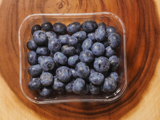 A plastic tray of blueberries sits on a wooden table. The tray is clear and filled with fresh organic fruits ready for consumption. Healthy diet concept. Natural product.