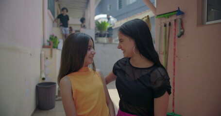 Two young Hispanic Latin girls hugging and laughing in suburban alleyway, joyful and playful...