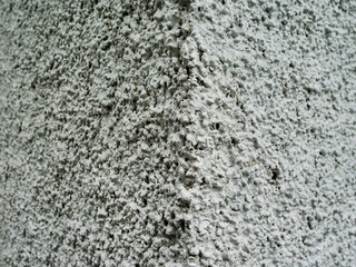 A corner of a plastered wall is covered in white paint. The texture of the paint is rough and bumpy, giving the wall a somewhat rugged appearance