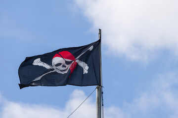 Black pirate flag waving against blue sky