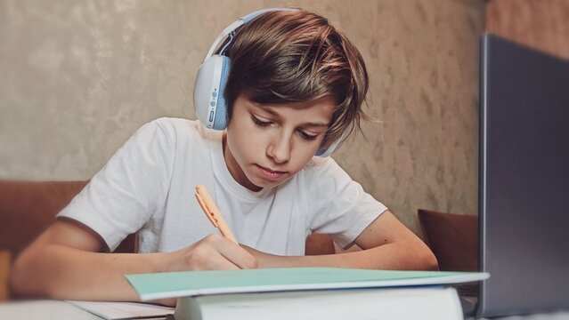 Boy Uses Laptop for Learning, Writes Down Useful Information. Distance Learning, e-Education, Homeschooling Concept. Portrait of a Boy Doing Homework - Powered by Adobe