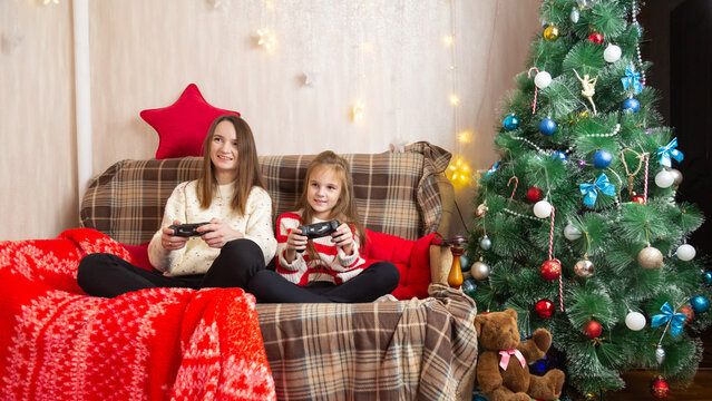 Happy family mother and daughter laugh and play video games together using a video game console on christmas holiday