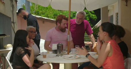 Older man standing and interacting with a group during an outdoor lunch, fostering community and...