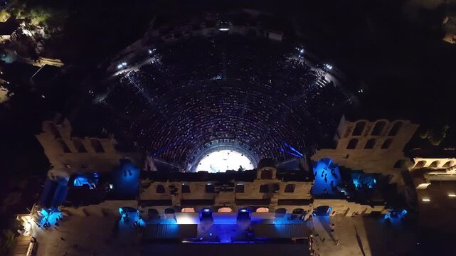 Aerial drone cinematic night video of iconic illuminated ancient Odeon of Herodes Atticus during summer music festival, Athens, Greece