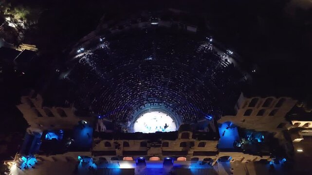 Aerial drone cinematic night video of iconic illuminated ancient Odeon of Herodes Atticus during summer music festival, Athens, Greece