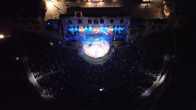 Aerial drone cinematic night video of iconic illuminated ancient Odeon of Herodes Atticus during summer music festival, Athens, Greece