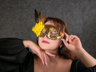 Portrait of a beautiful woman of 40-50 years old wearing a golden carnival mask and a black dress