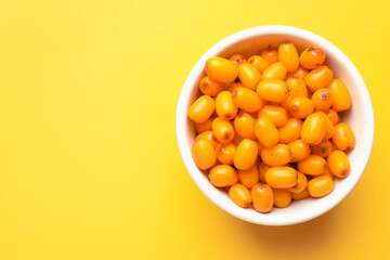 Ripe sea buckthorn berries in bowl on yellow background, top view. Space for text