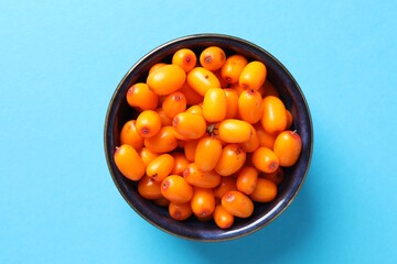 Ripe sea buckthorn berries in bowl on light blue background, top view