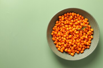 Ripe sea buckthorn berries and leaves in bowl on green background, top view. Space for text