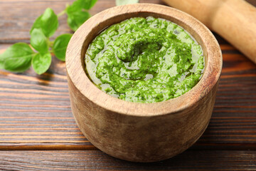 Fresh pesto sauce in mortar, pestle and basil leaves on wooden table, closeup