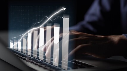 A close-up view of hands typing on a laptop, accompanied by a digital graph illustrating an upward...