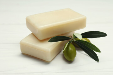 Natural soap bars with olives and green leaves on white wooden table, closeup