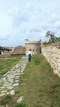 Smiling woman walking alone beside Belgrade Fortress walls and battlement towers of Zindan Gate. Concepts of joyful travel, solo tourism, cultural authenticity in Serbia, Balkan architectural heritage