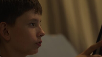 An 11-year-old Caucasian boy is diligently using a tablet computer while at home. The teenager spends time with the gadget solving everyday problems. - Powered by Adobe
