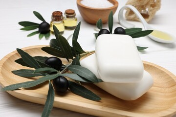 Handmade soap bars, olives, green leaves, essential oils, sea salt and loofah on white wooden table, closeup