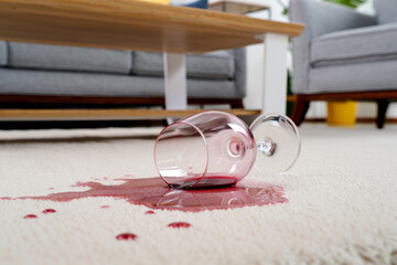 A glass of red wine tips over, spilling liquid across the surface, creating a household accident with dramatic splashing motion.