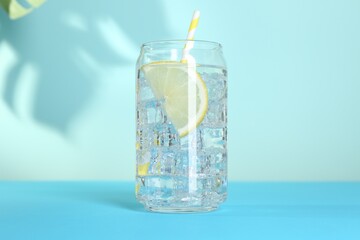 Refreshing water with lemon and ice on light blue background, closeup